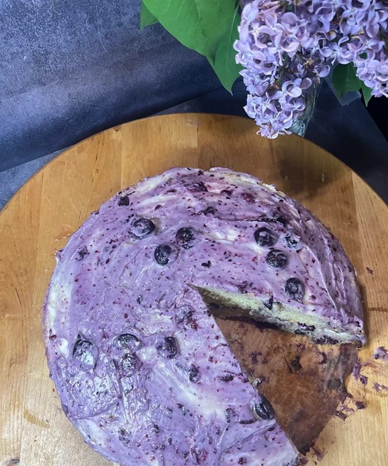 A blueberry cheesecake with a slice removed on a wooden board.