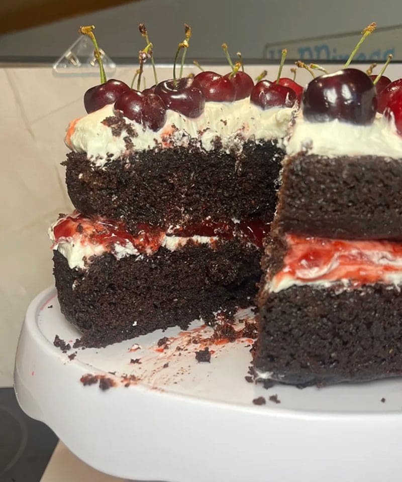Slices of rich chocolate cake topped with cream and cherries on a white plate.