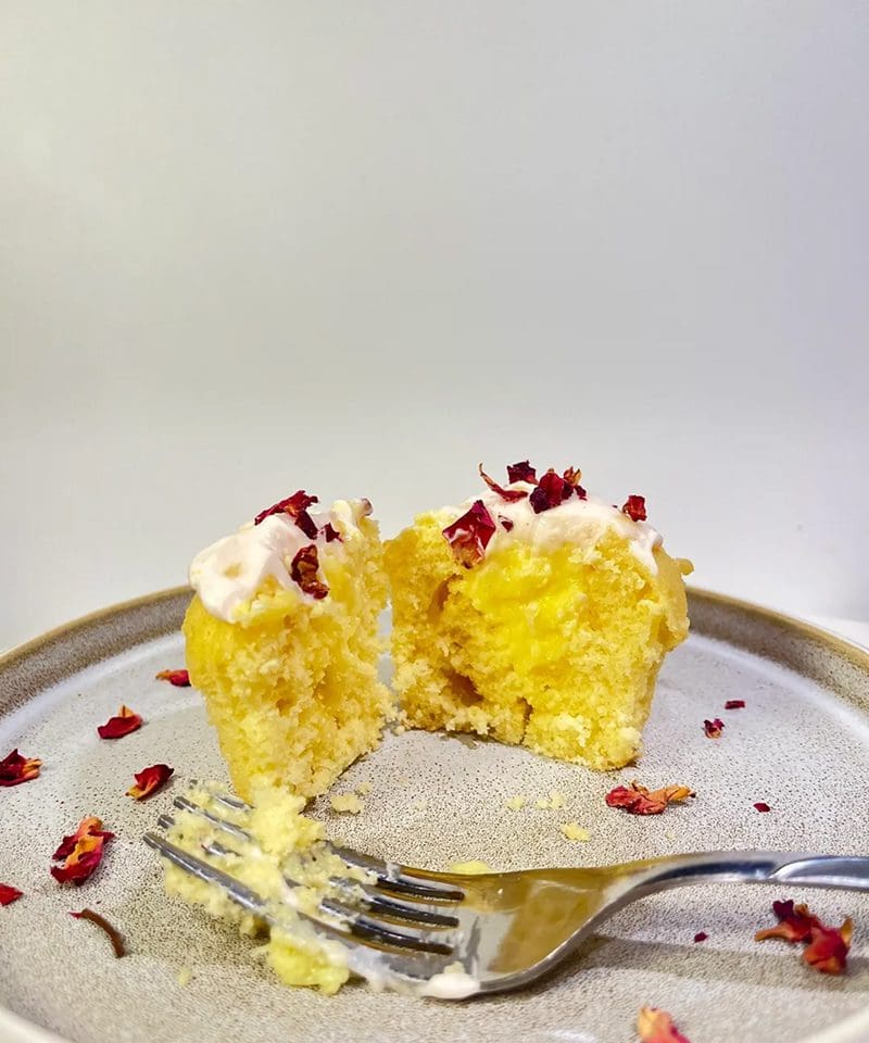 A moist yellow cupcake with cream and red sprinkles, partially eaten.
