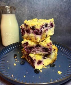 Blueberry crumb bars stacked on a plate with a bottle of milk.