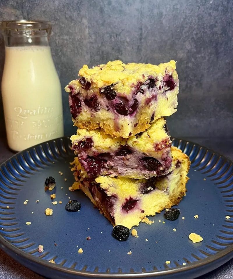 Blueberry crumb bars stacked on a plate with a bottle of milk.