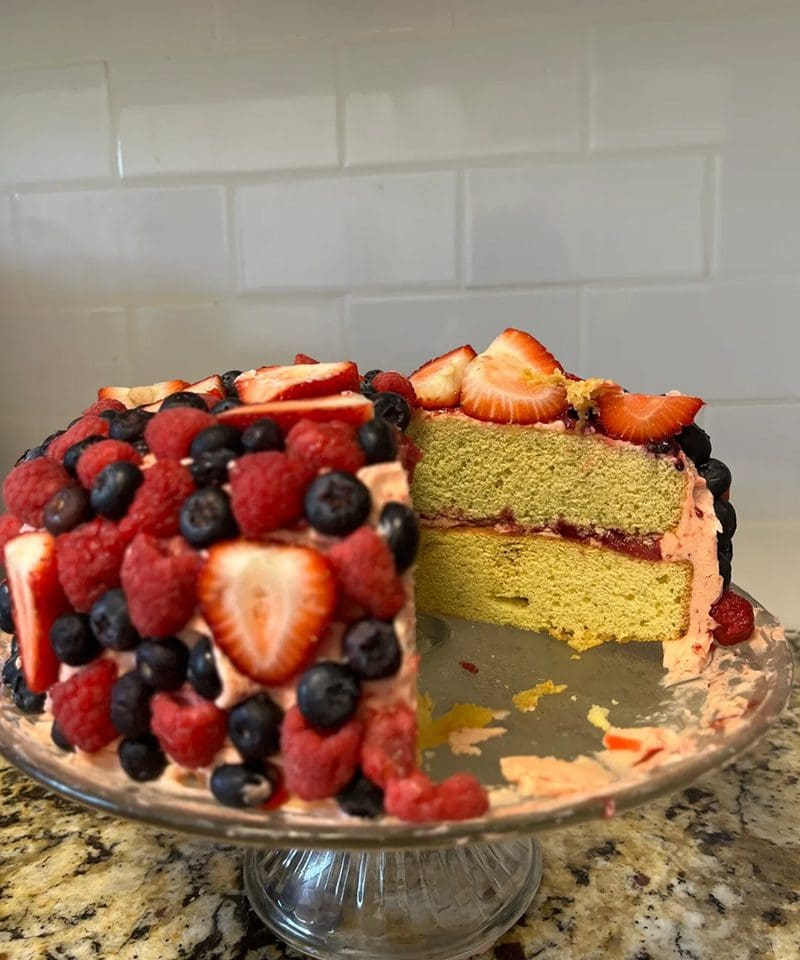 A fruit-covered layered cake with strawberries and blueberries.