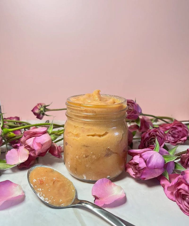 A jar of creamy, light brown spread surrounded by pink rose petals.