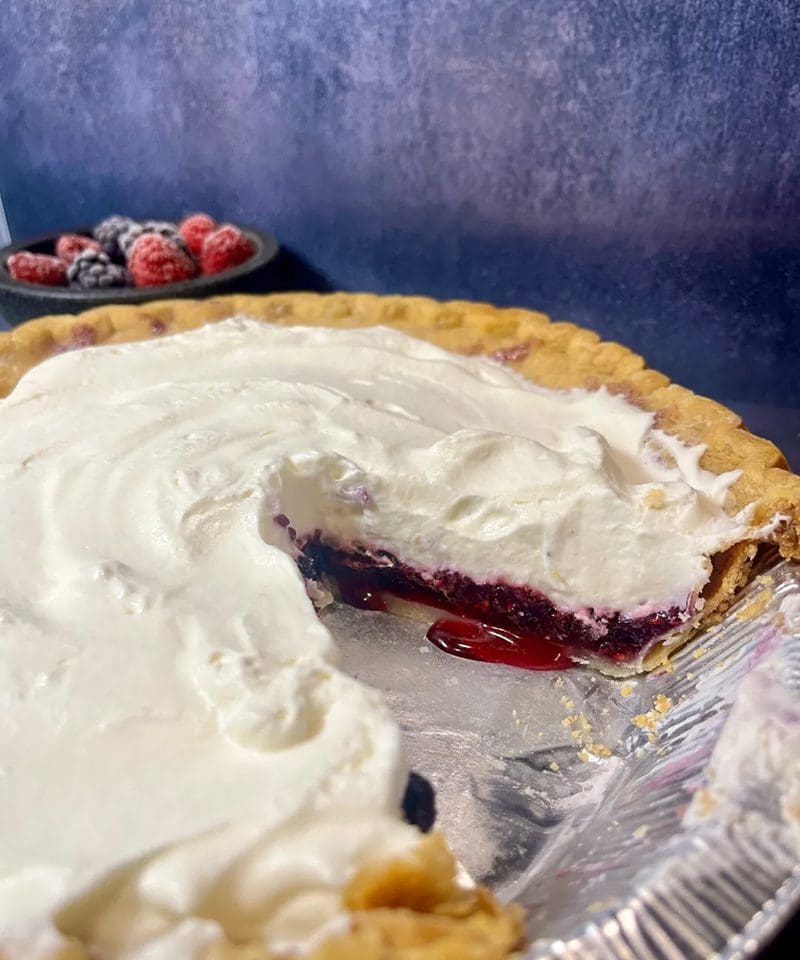 A cherry pie with whipped cream and a slice removed.