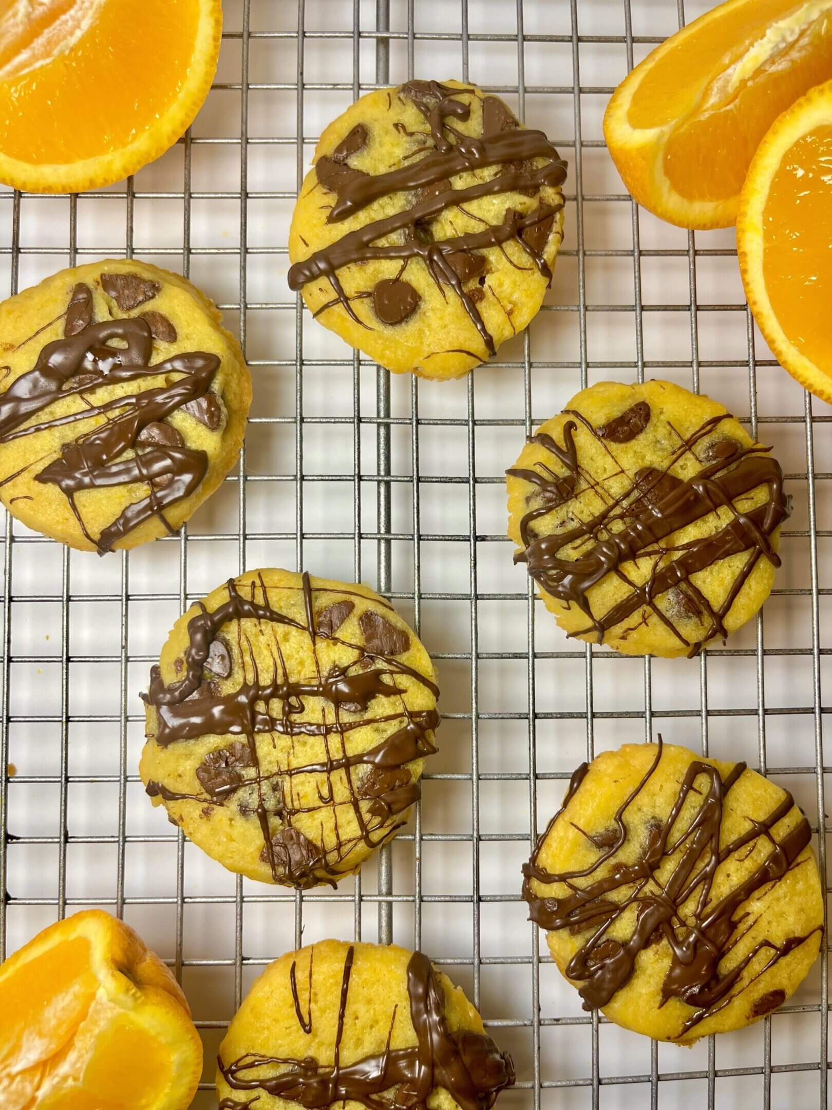 Orange cookies with chocolate drizzle on rack.