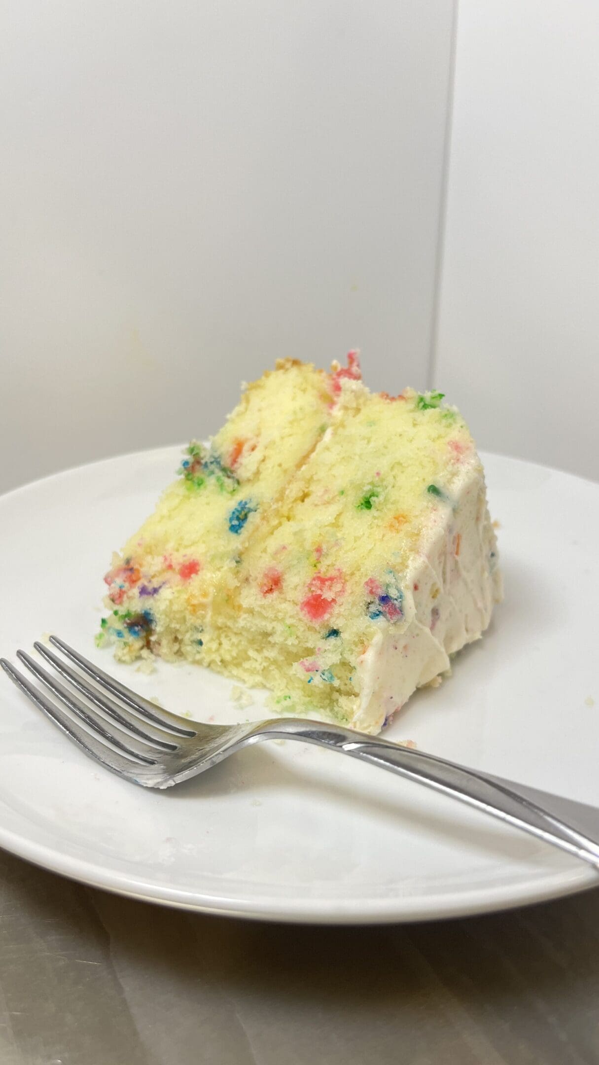 Slice of confetti cake on white plate.