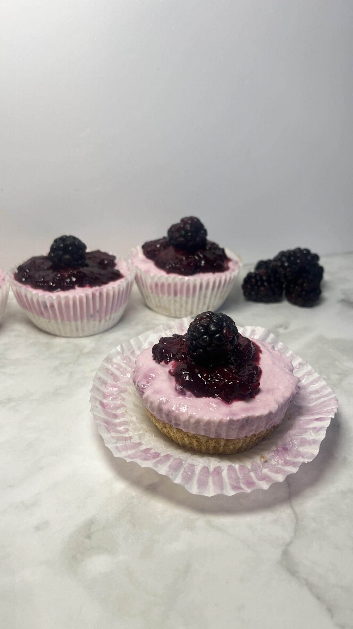 Mini blackberry cheesecakes on marble surface.