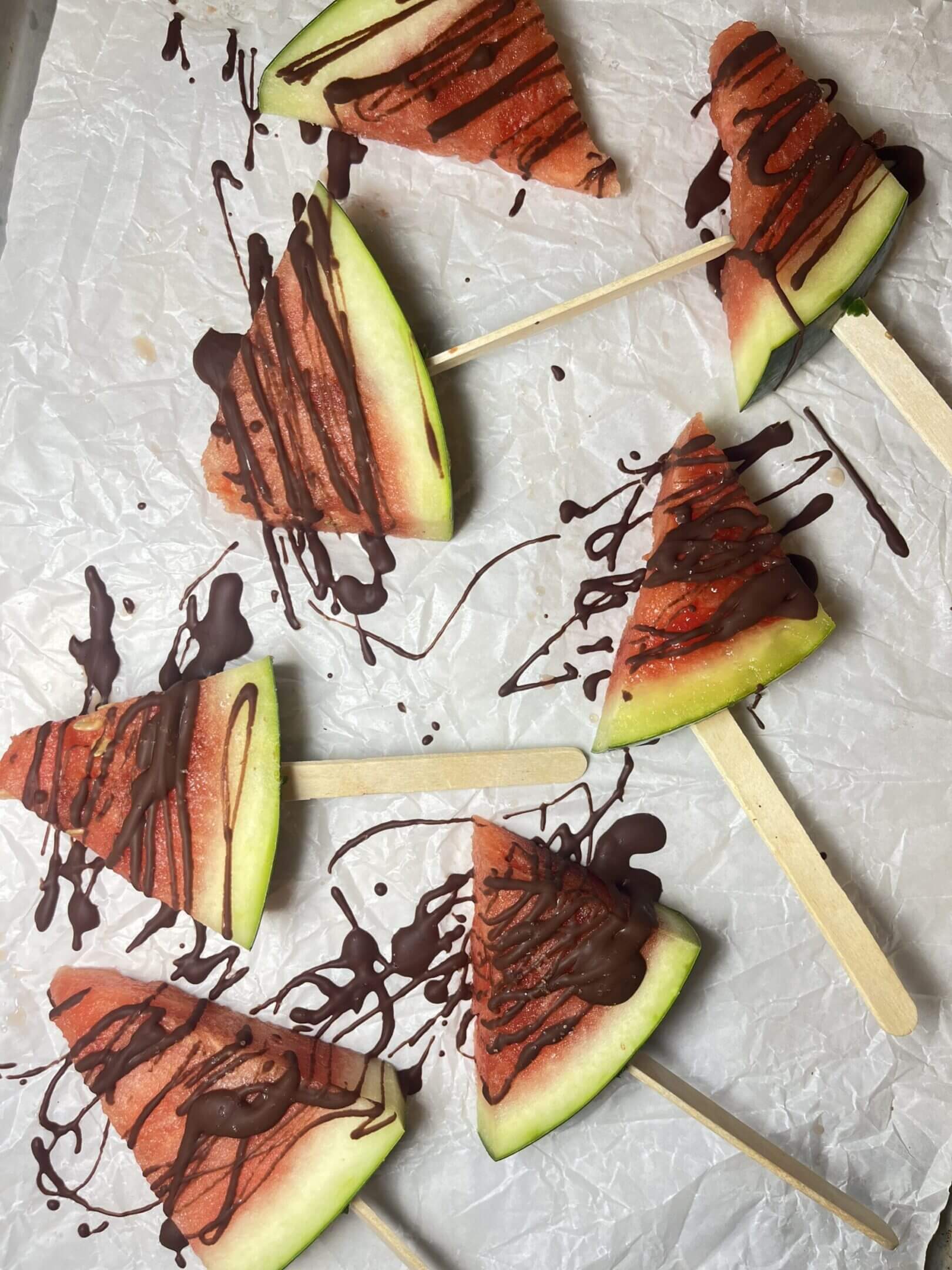 Watermelon slices on sticks with chocolate drizzle.