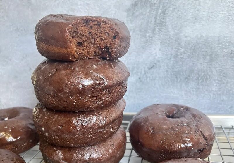 A stack of chocolate donuts with a few more on the side on a wire rack.