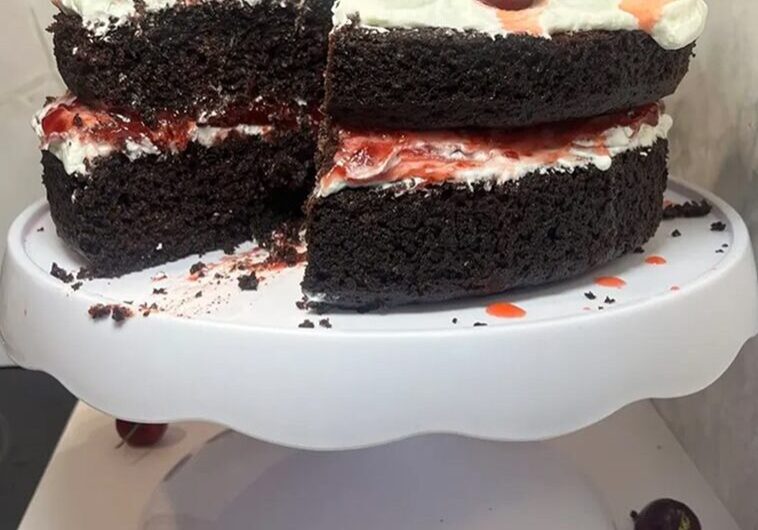 Chocolate cake slices with cherries on top on a white cake stand.