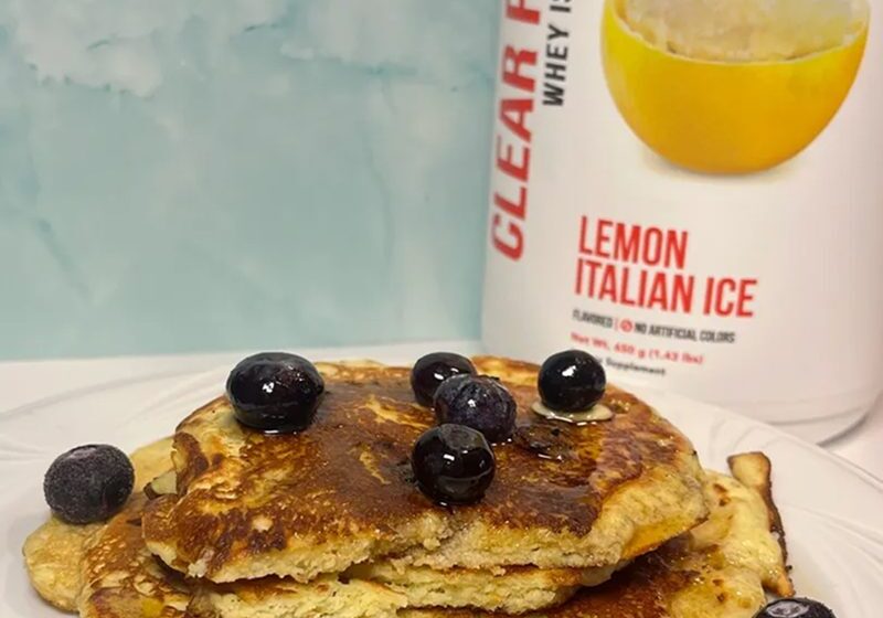 Stack of pancakes topped with blueberries and syrup beside a lemon Italian ice.