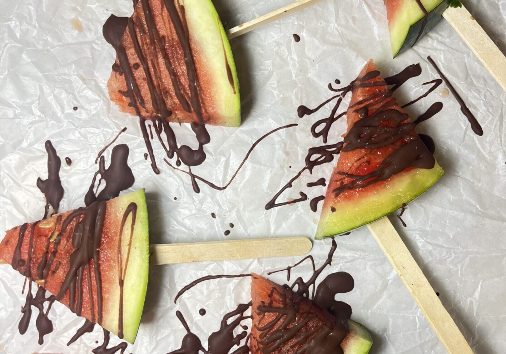 Watermelon slices on sticks with chocolate drizzle.