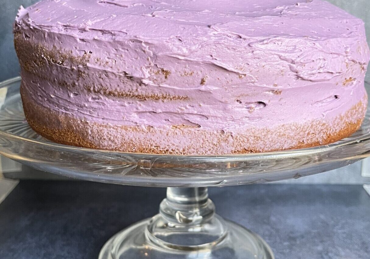 Purple-frosted cake on a glass stand.