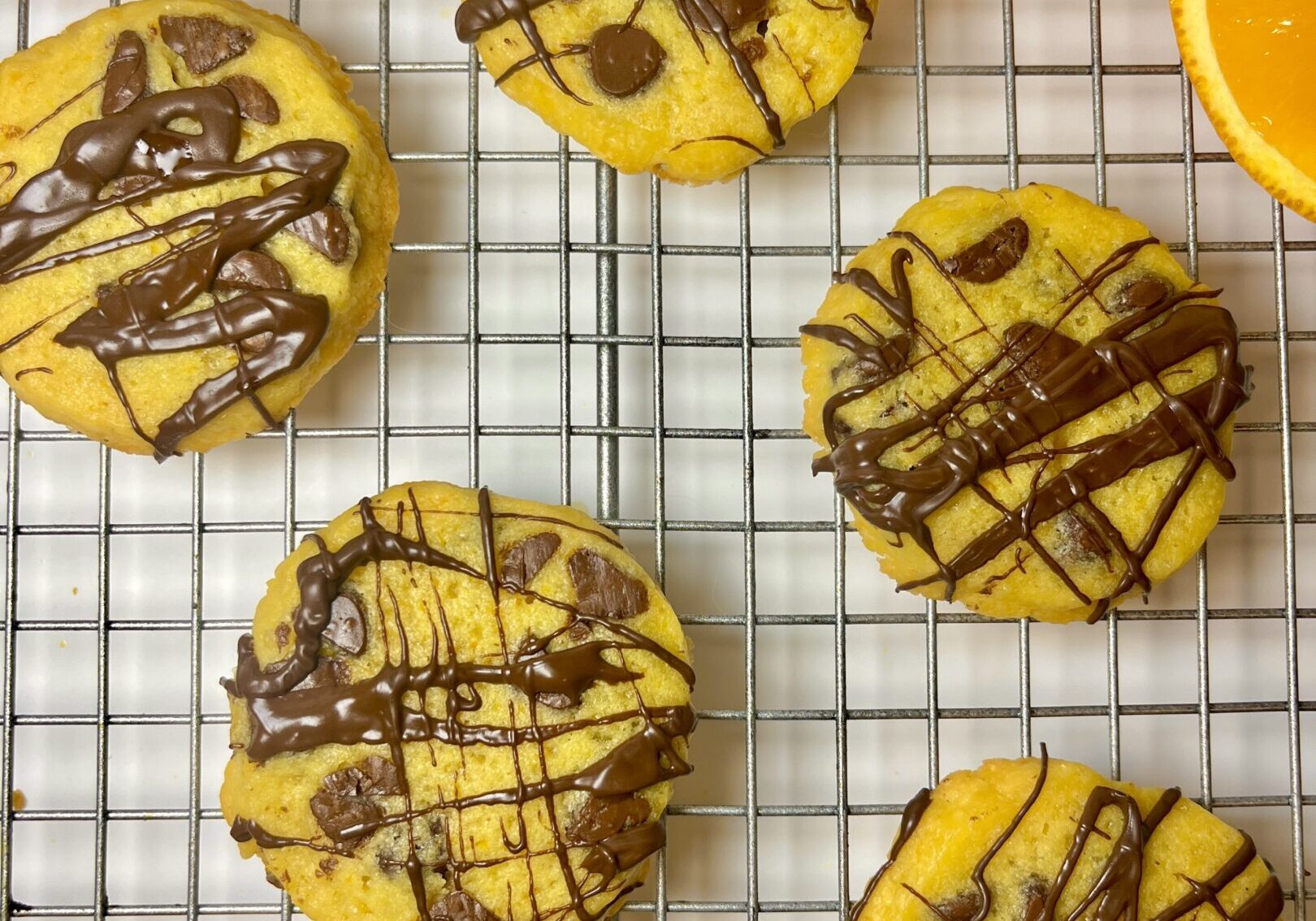 Orange cookies with chocolate drizzle on rack.