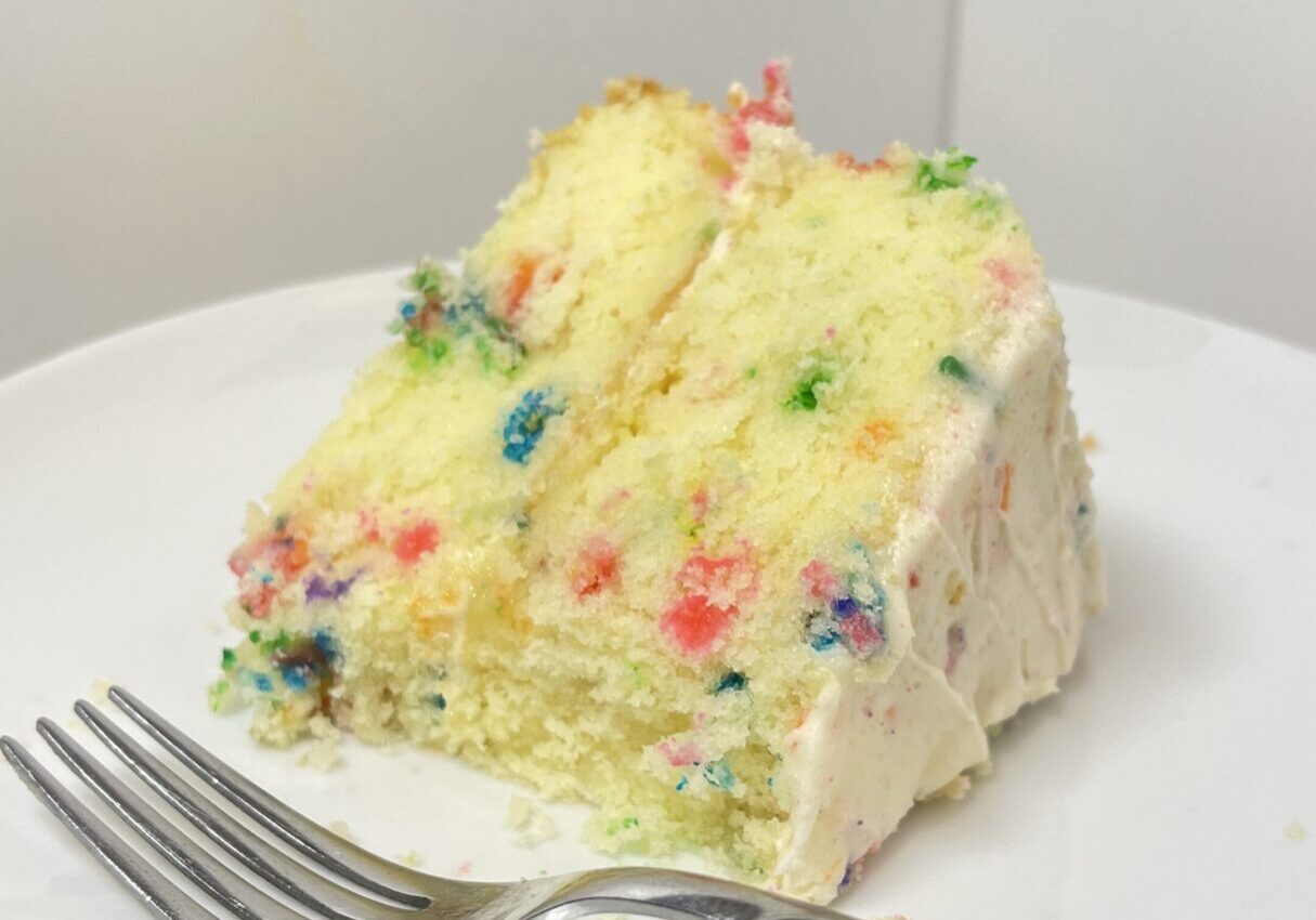 Slice of confetti cake on white plate.