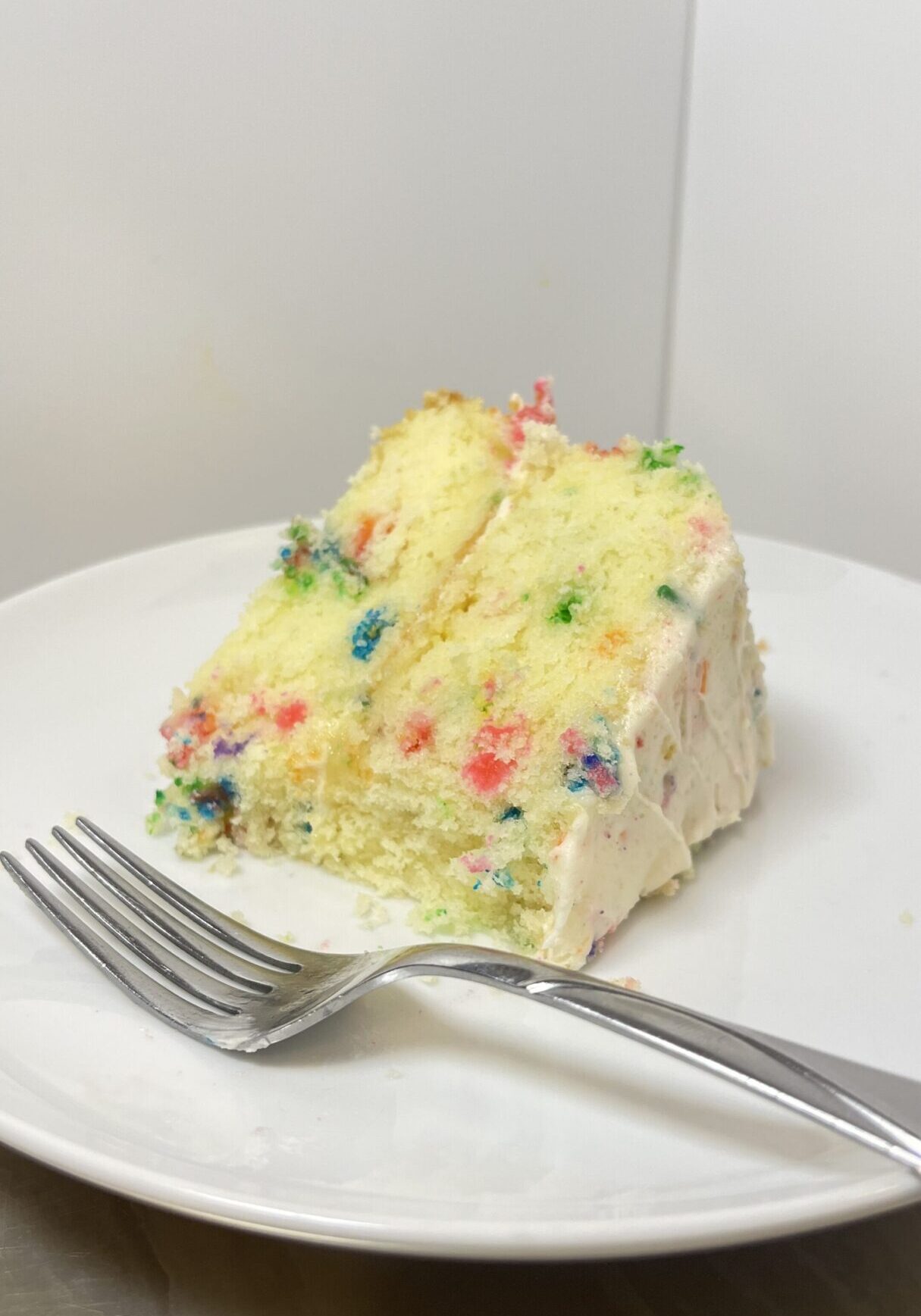 Slice of confetti cake on white plate.