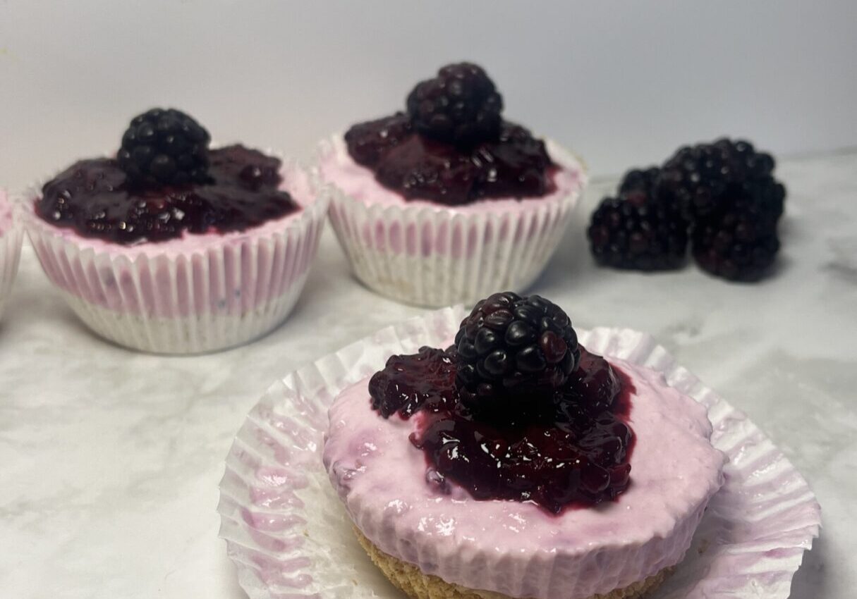 Mini blackberry cheesecakes on marble surface.