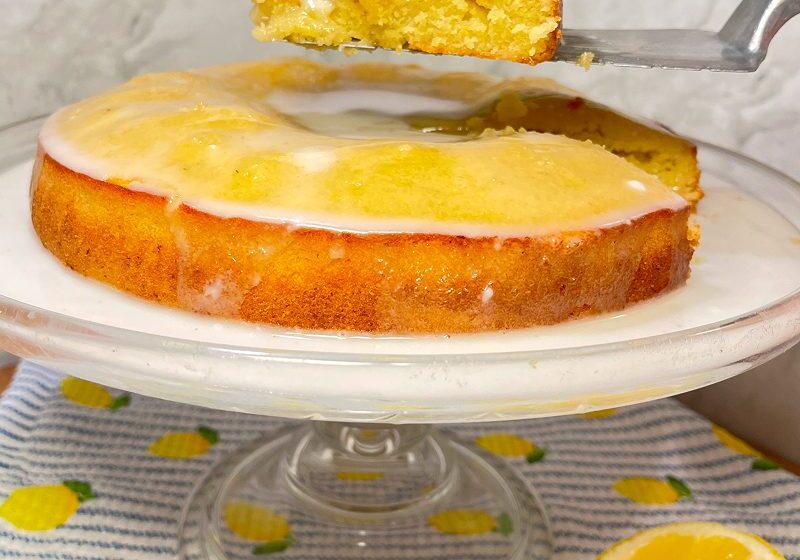 Lemon cake with a slice being lifted, topped with a glossy glaze.