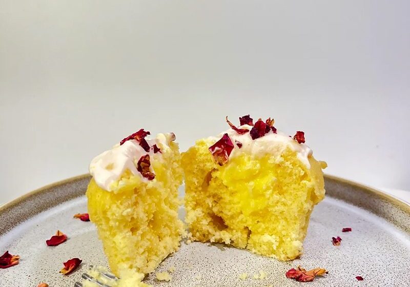 A moist yellow cupcake with cream and red sprinkles, partially eaten.