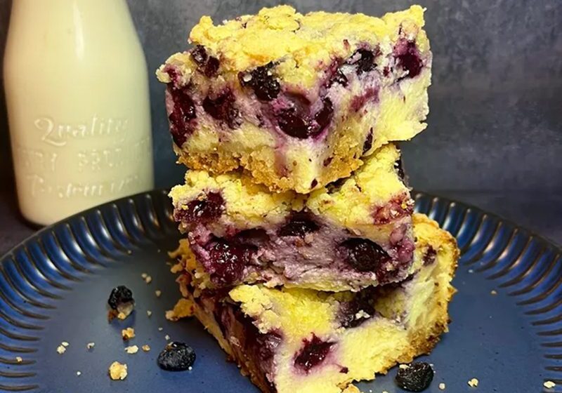 Blueberry crumb bars stacked on a plate with a bottle of milk.
