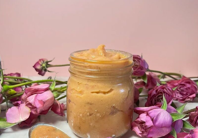 A jar of creamy, light brown spread surrounded by pink rose petals.
