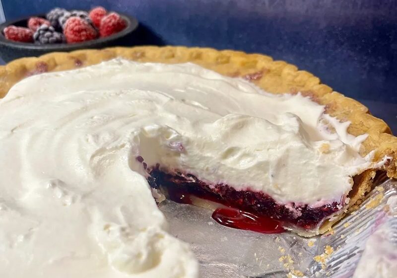 A cherry pie with whipped cream and a slice removed.